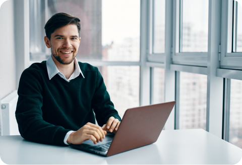 Smiling engineer working on a laptop beside an office window